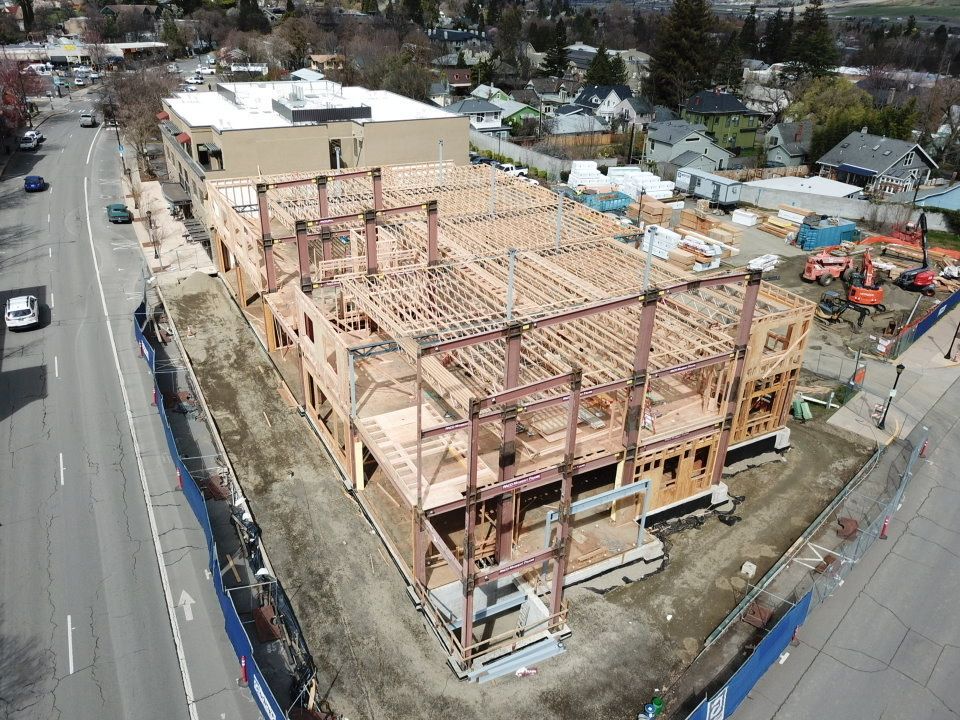 Construction site of a two-story building. Wood and steel frame visible. Street and buildings in the background.
