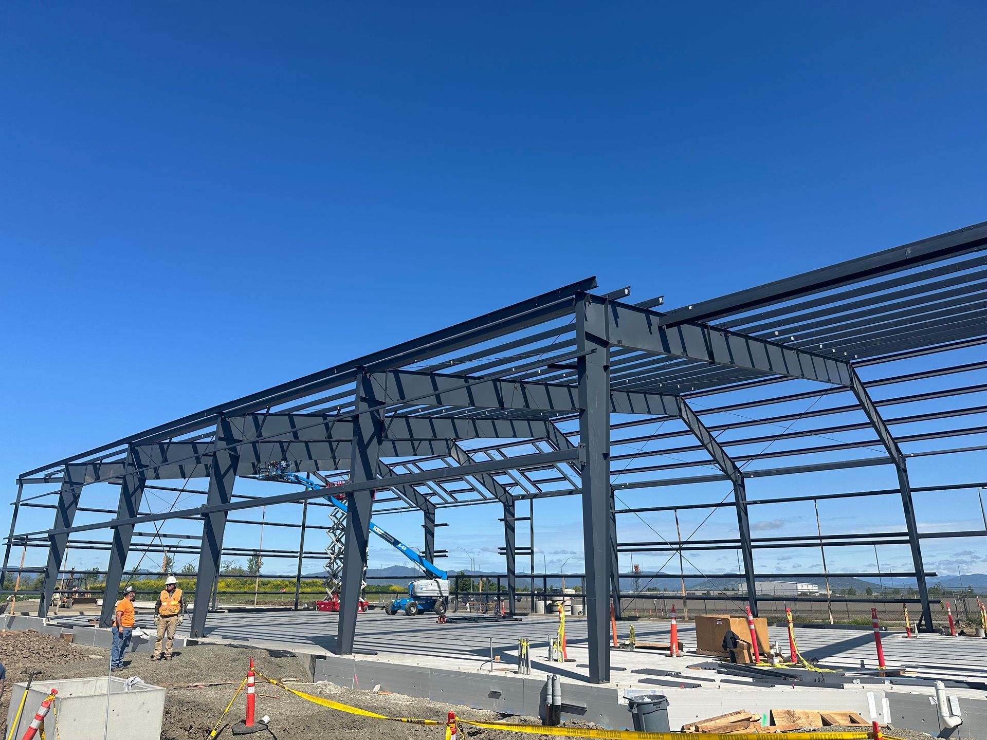 Steel framework of a building under construction on a sunny day; construction workers present.