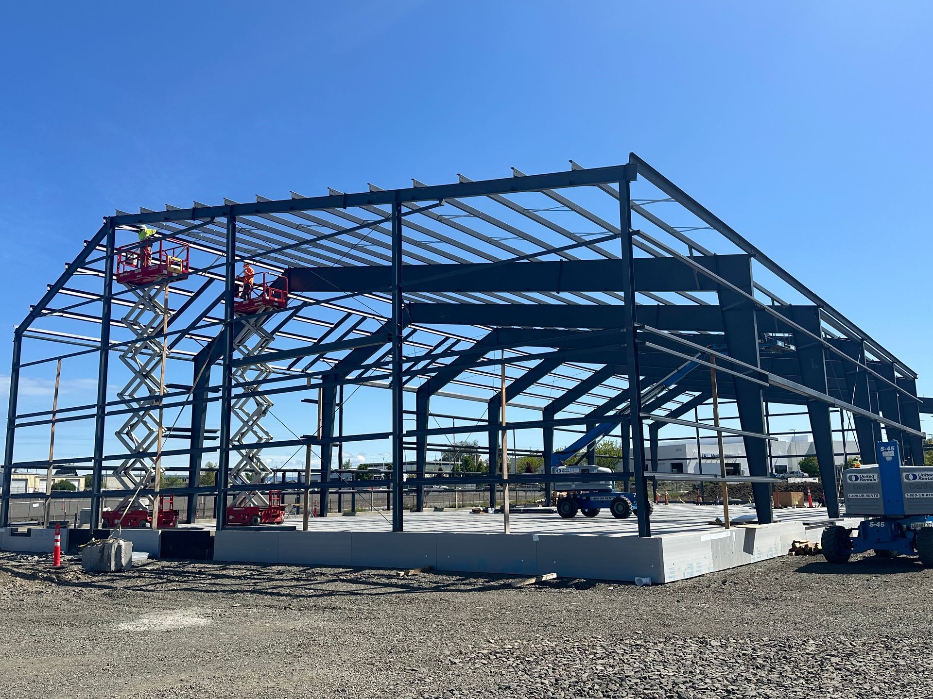 Steel structure of a building under construction; workers on lifts; blue sky.