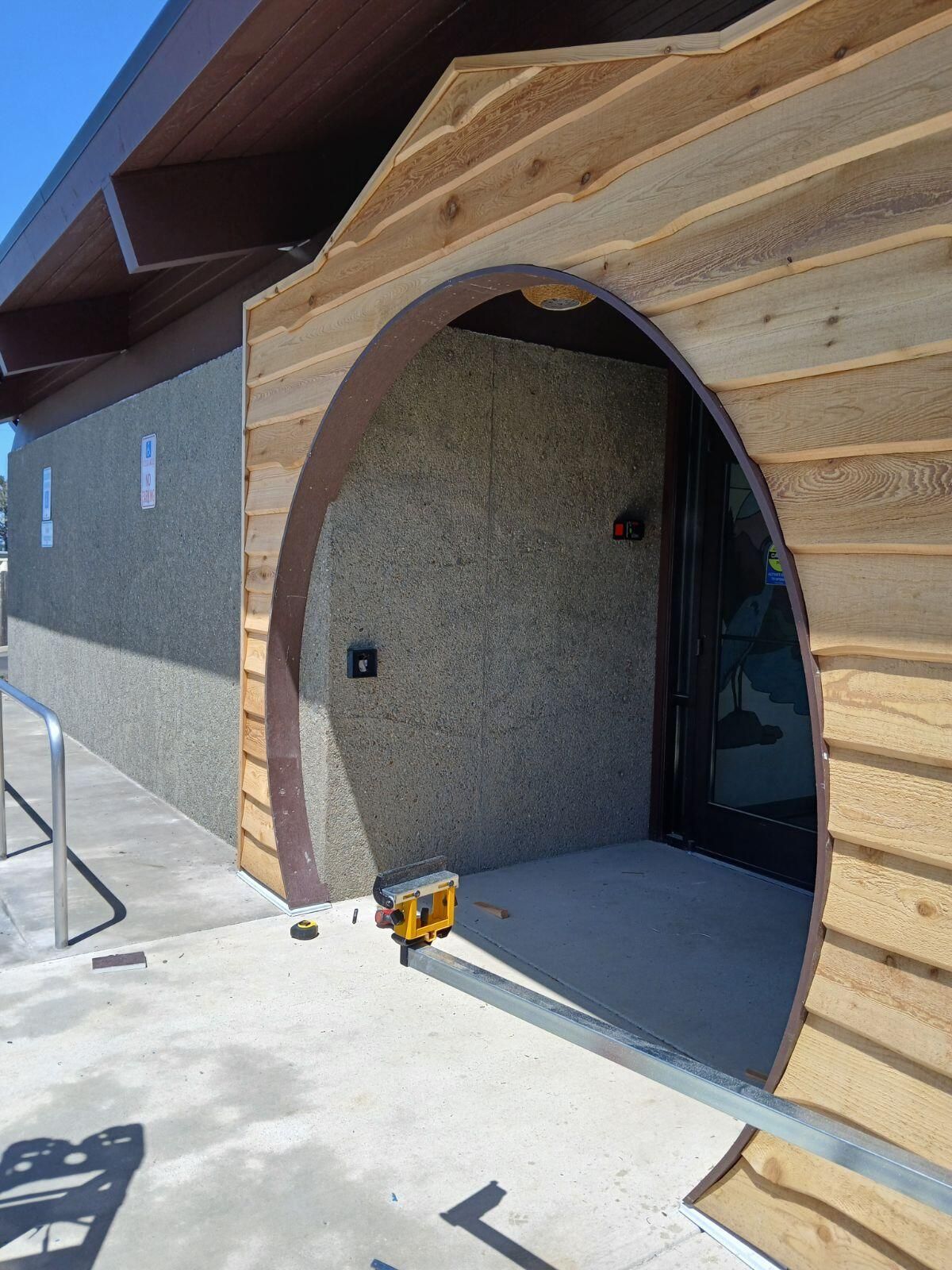 Entrance to a building with an arched doorway, surrounded by wood siding, on a concrete patio.