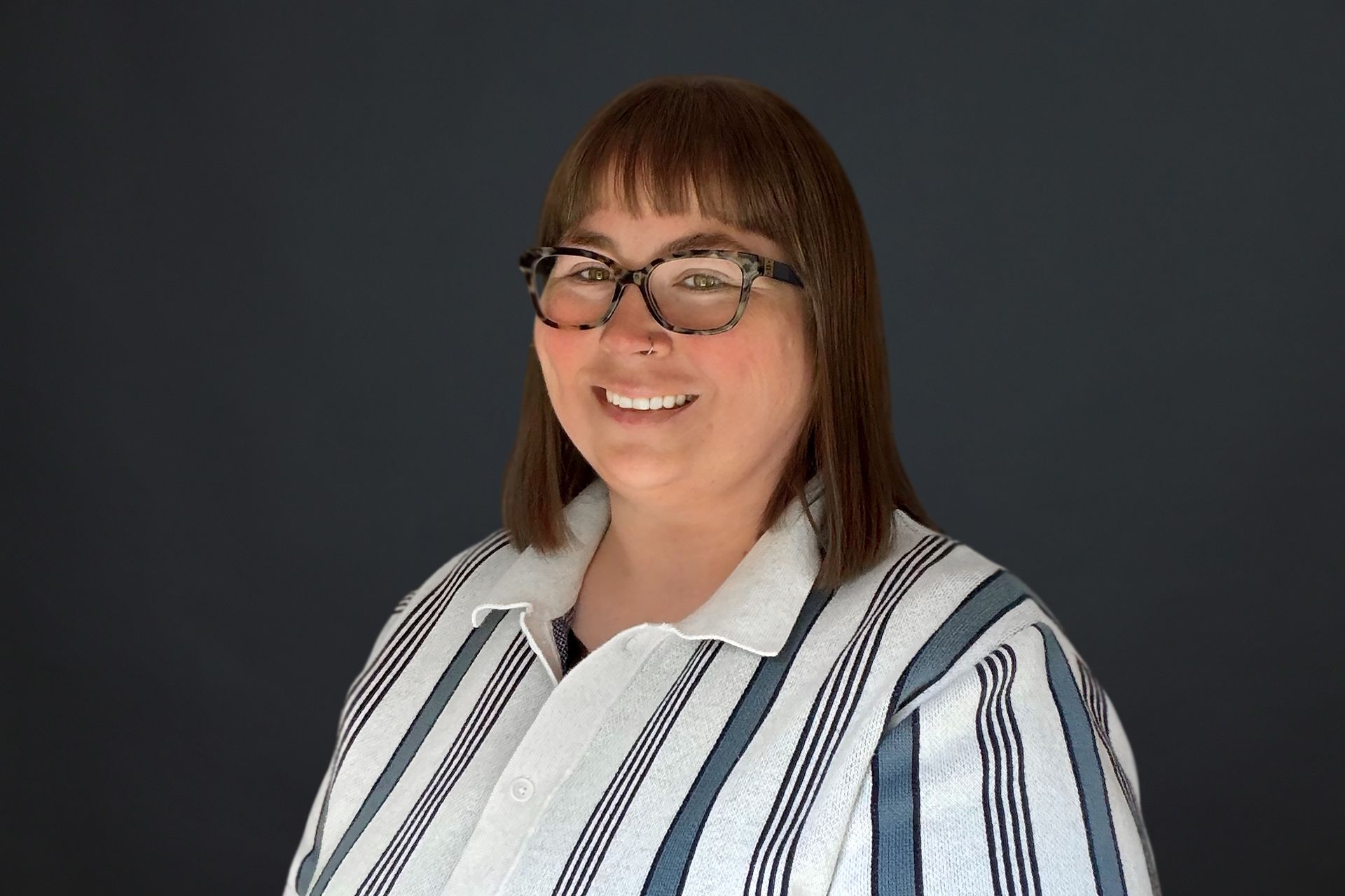 A woman wearing glasses and a black and white shirt is smiling for the camera.