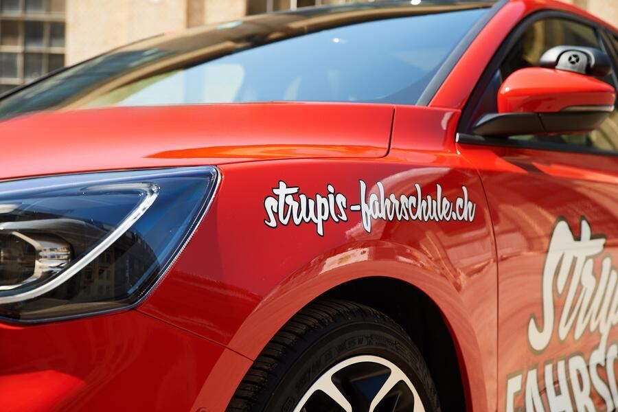 Ein rotes Auto mit einem Aufkleber auf der Seite mit der Aufschrift stripes-fahrschule.ch