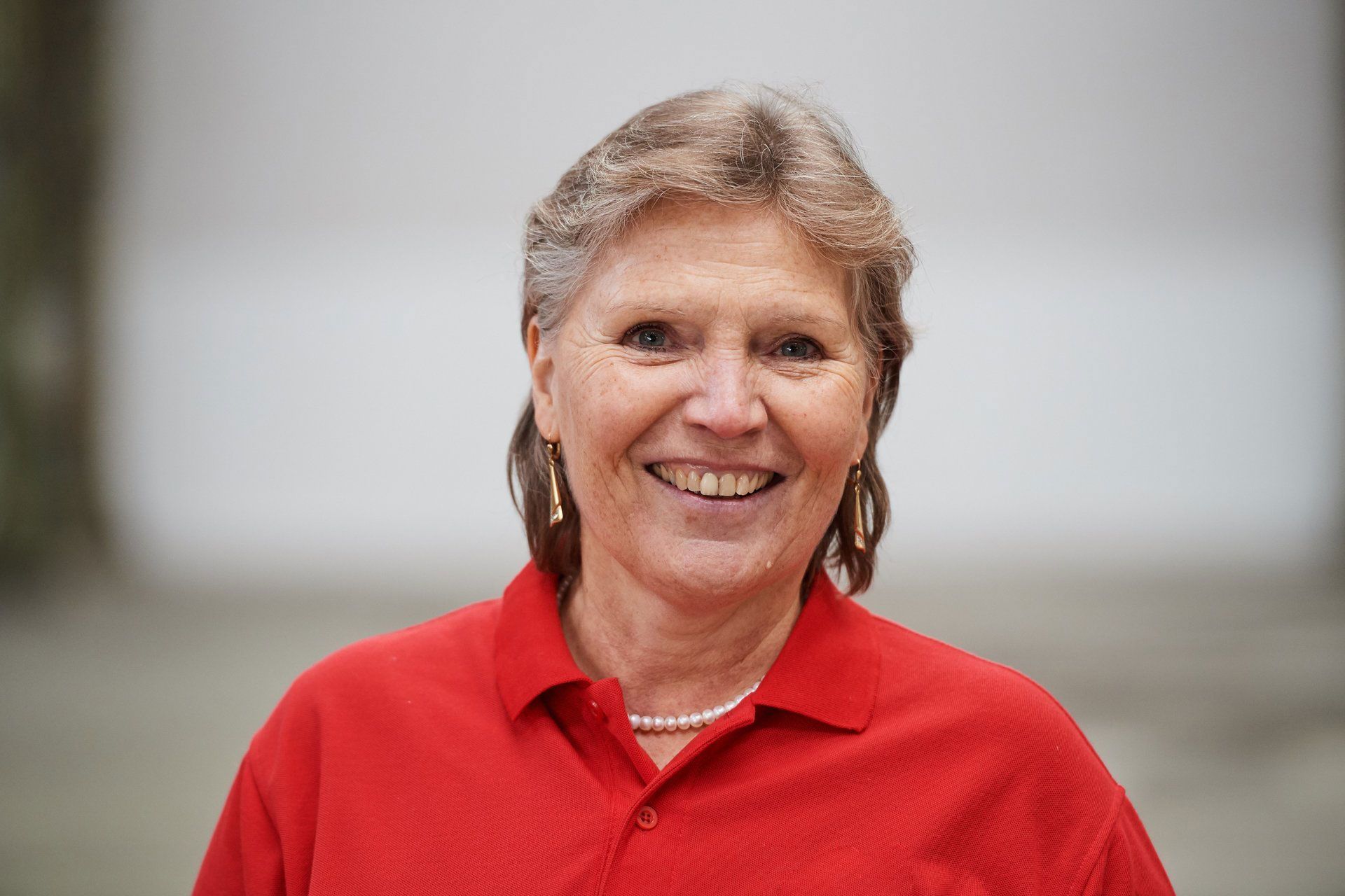 Lächelnde Person in einem roten Poloshirt vor verschwommenem neutralem Hintergrund
