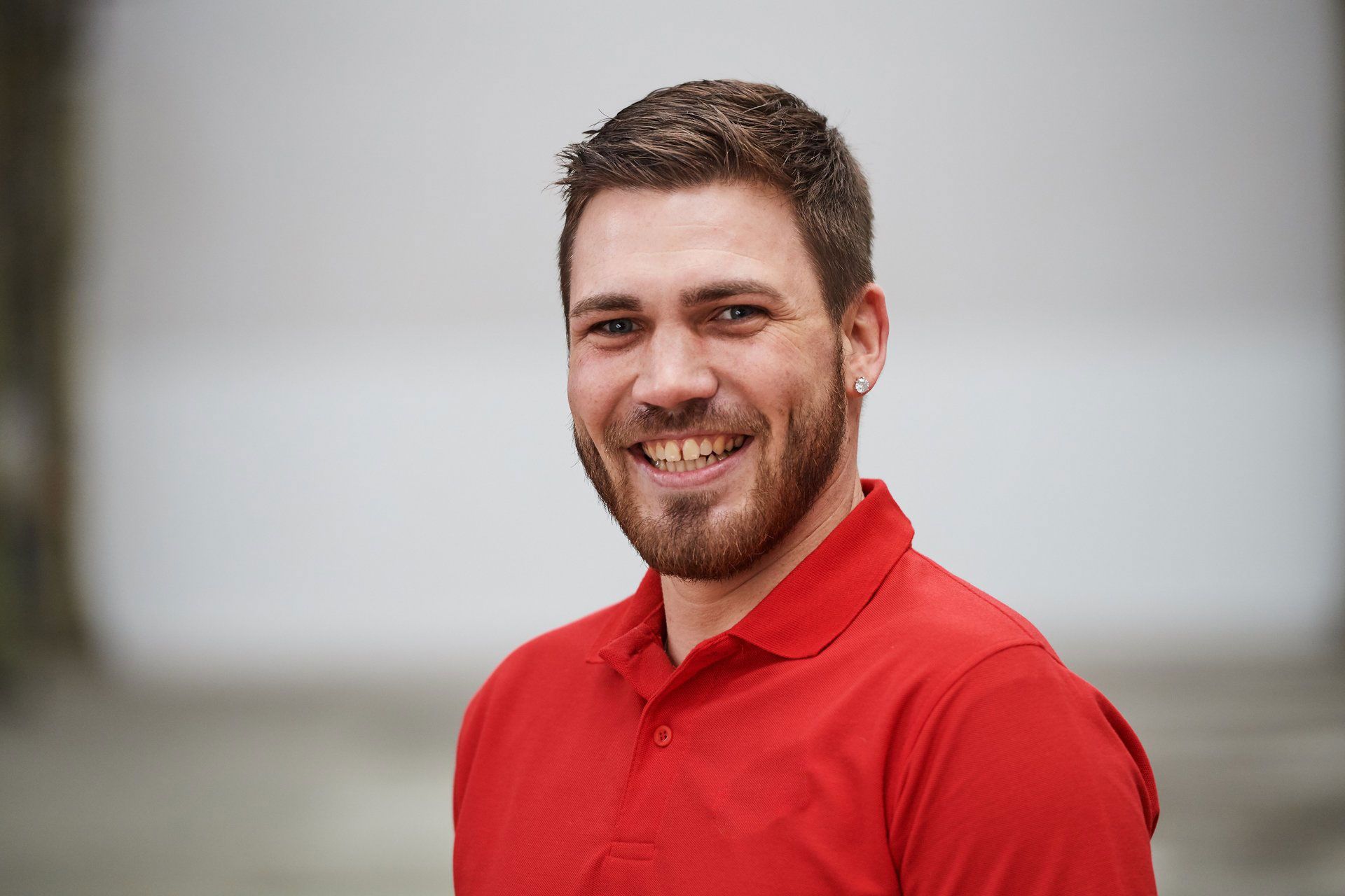 Lächelnder Mann in einem roten Poloshirt vor verschwommenem Hintergrund im Freien