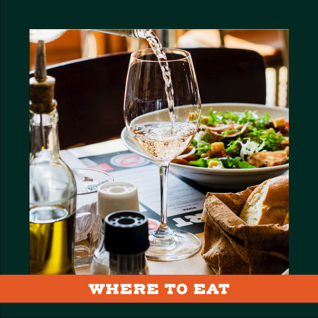 A glass of wine is being poured into a bowl of food on a table.
