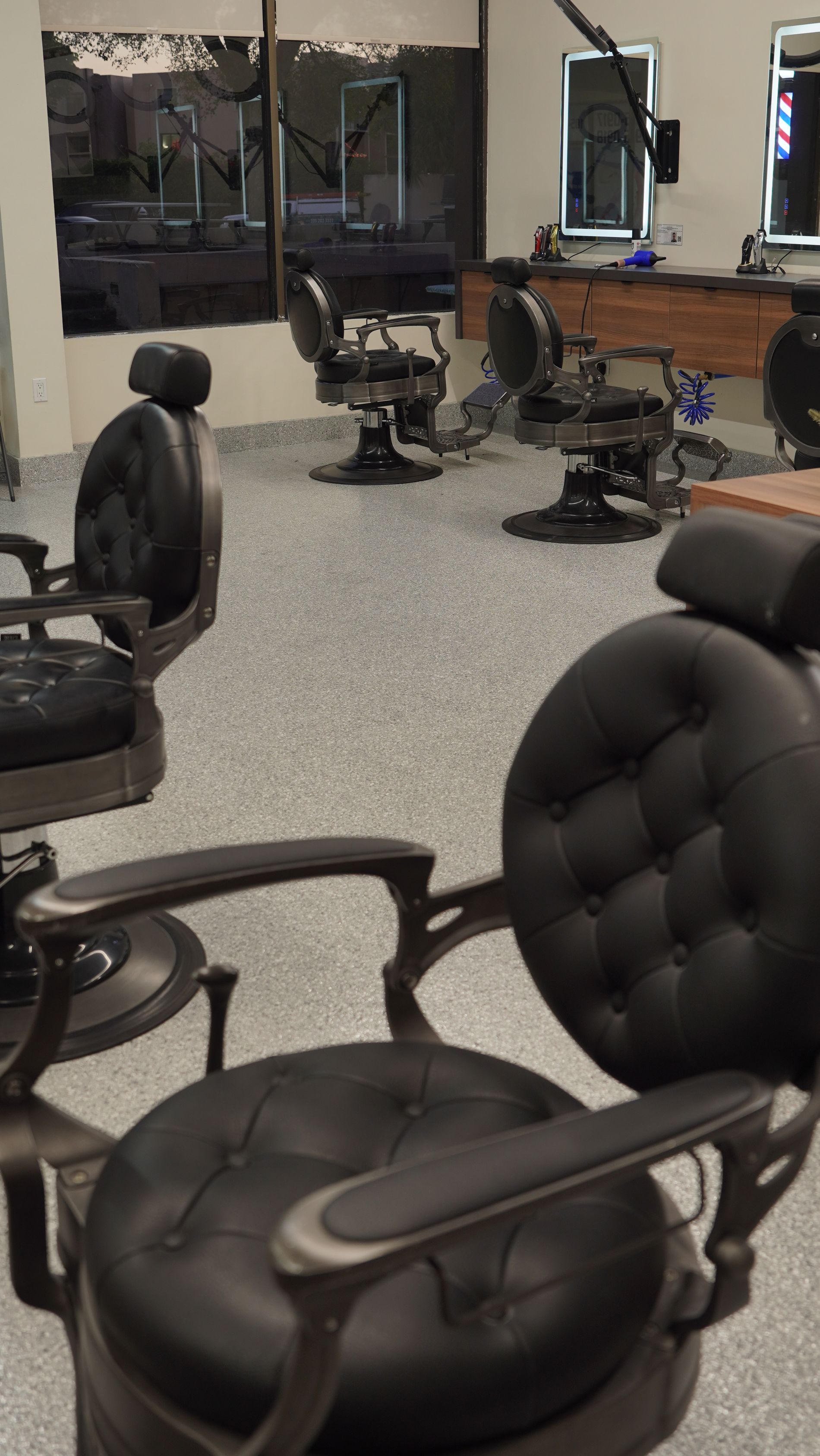 Barbershop interior with black leather chairs, mirrors, and speckled flooring.