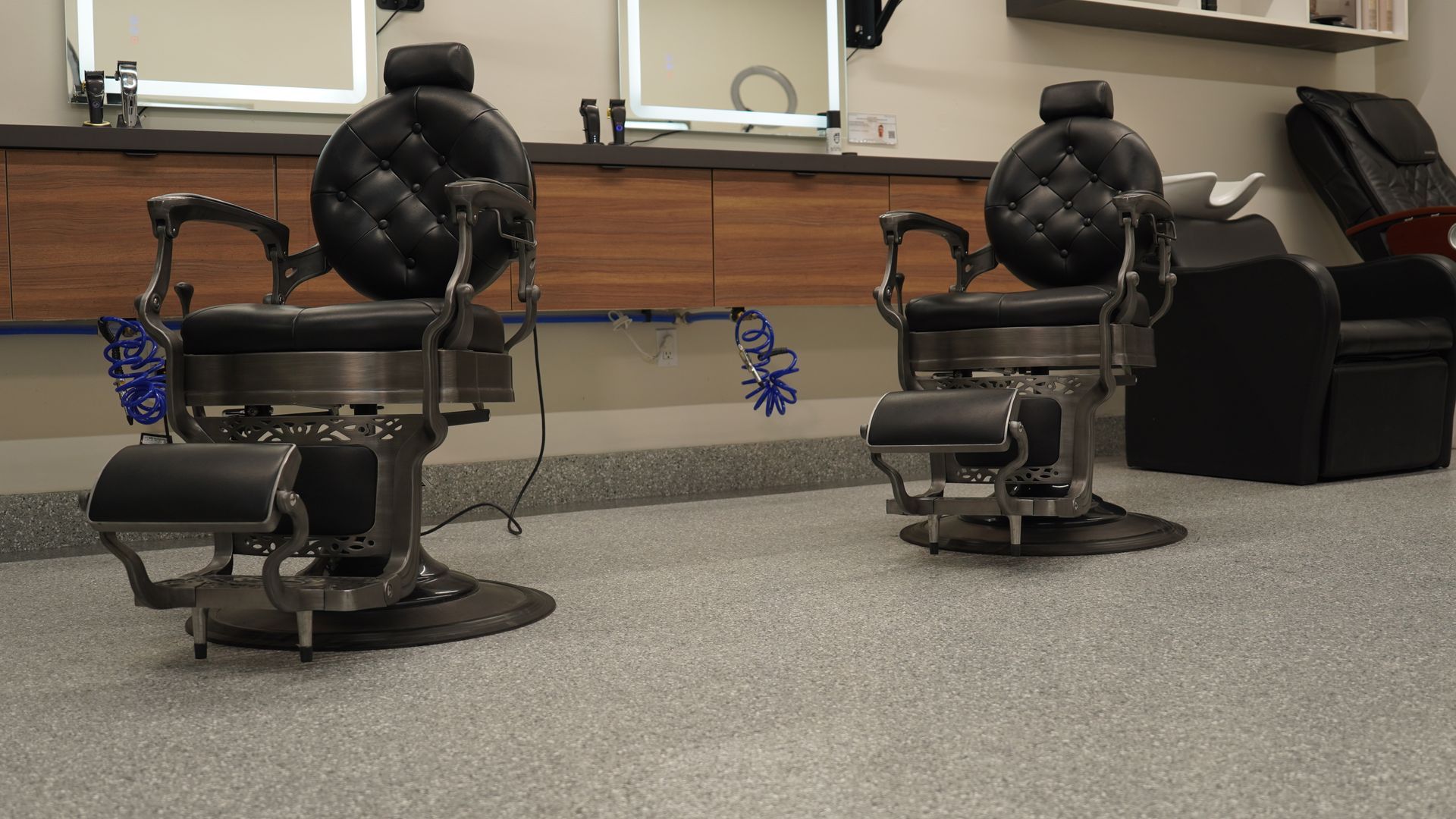 Two vintage barber chairs in a barbershop. Gray floor, wood cabinets, and mirrors in the background.