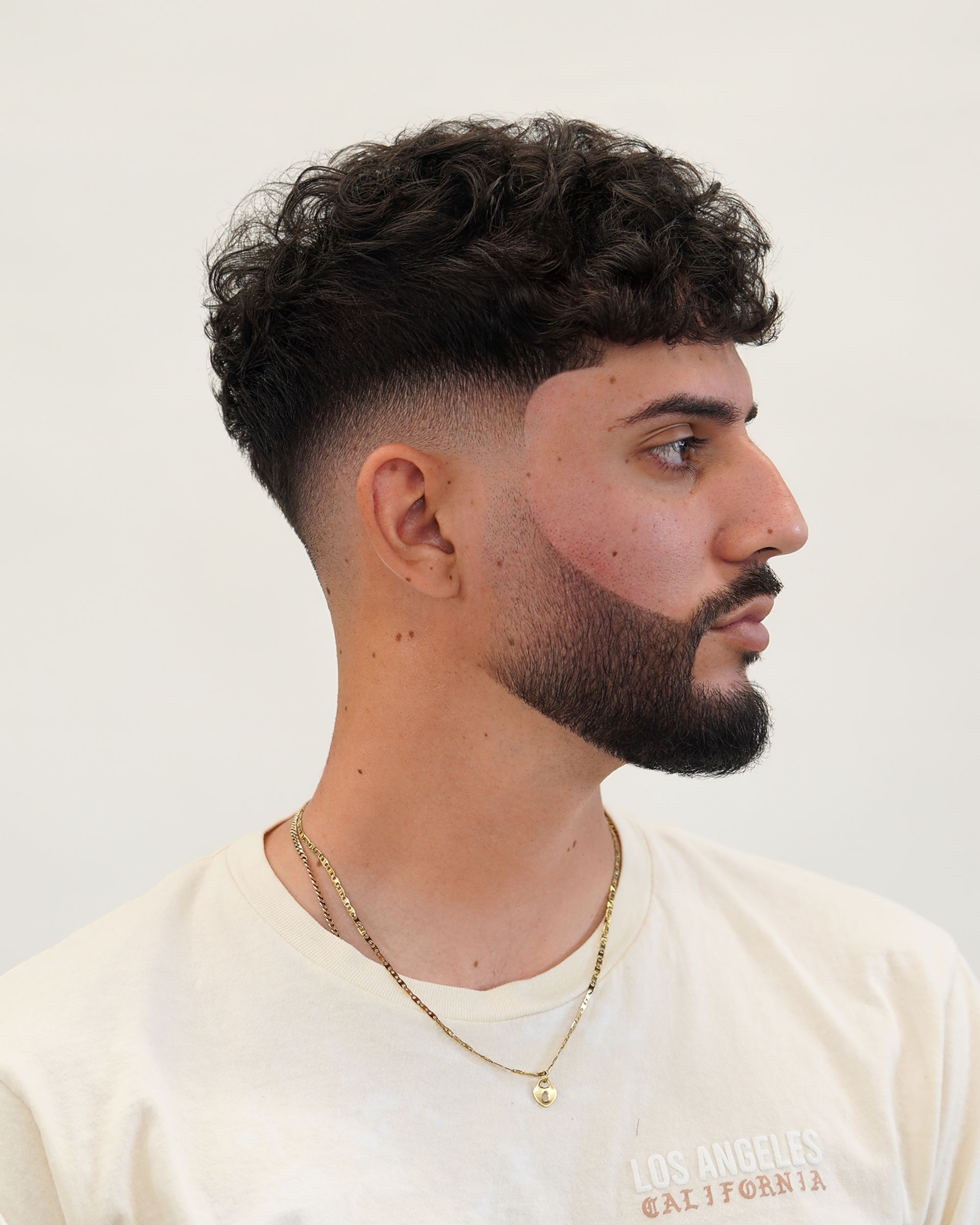 Man with curly hair and a fade haircut, wearing a cream shirt.