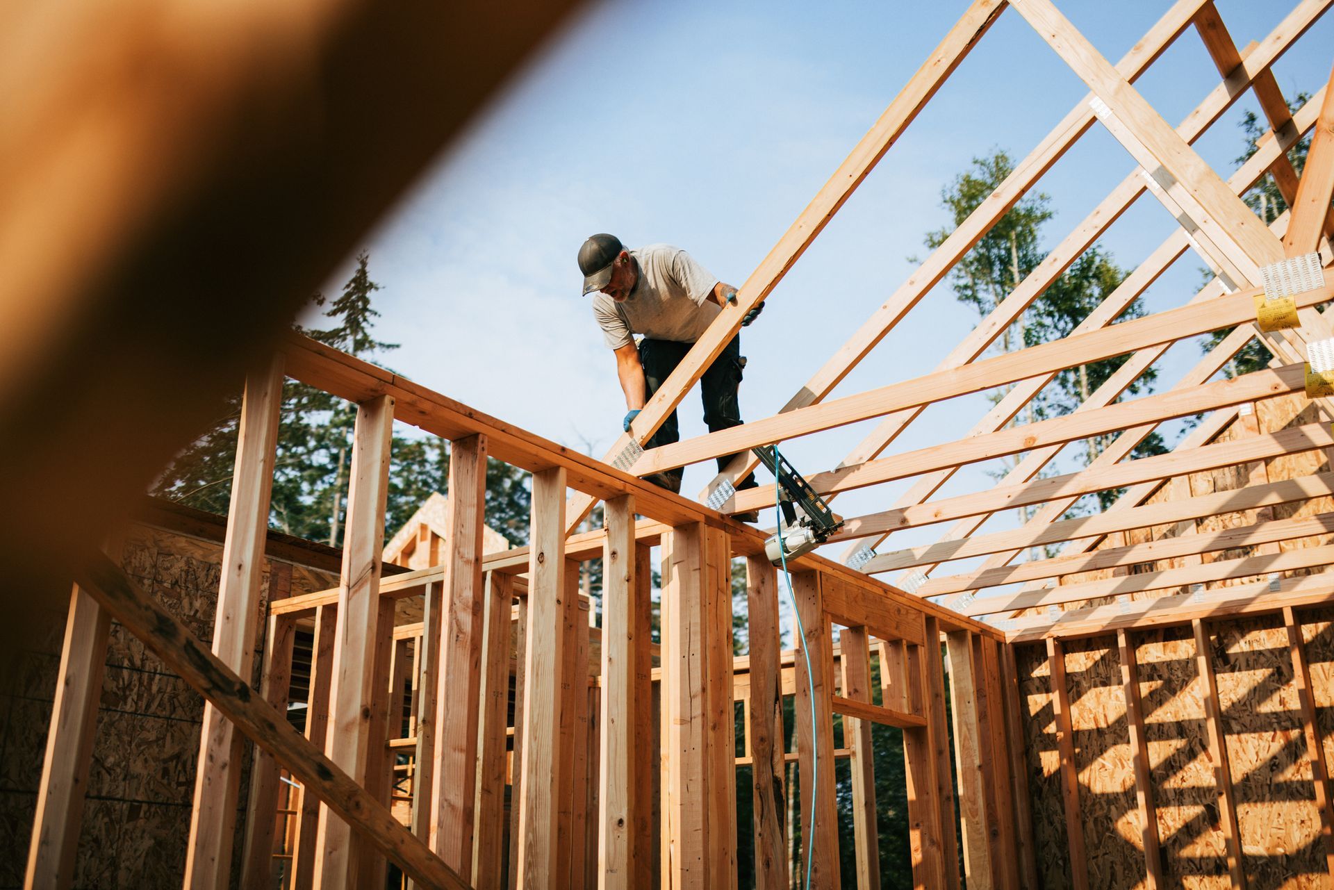 Man on the roof framing a house; blue sky, sunny day.