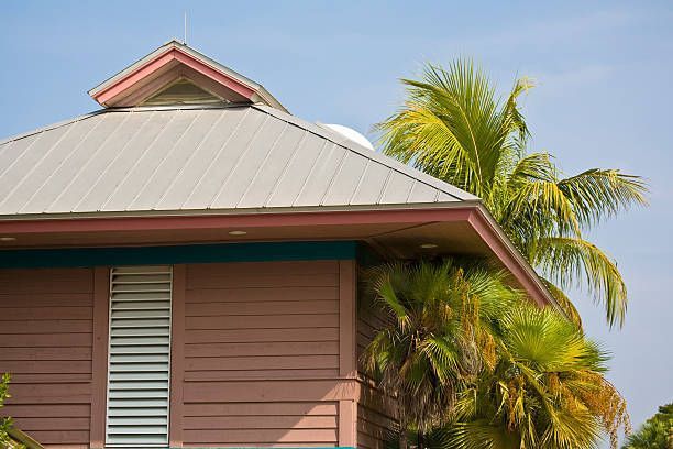Pink building with metal roof and palm trees against a blue sky.