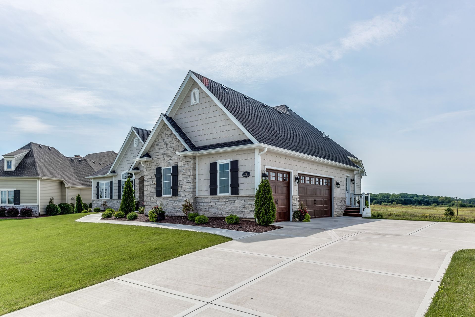 Beige brick house with a two-car garage and a long concrete driveway, under a blue sky.