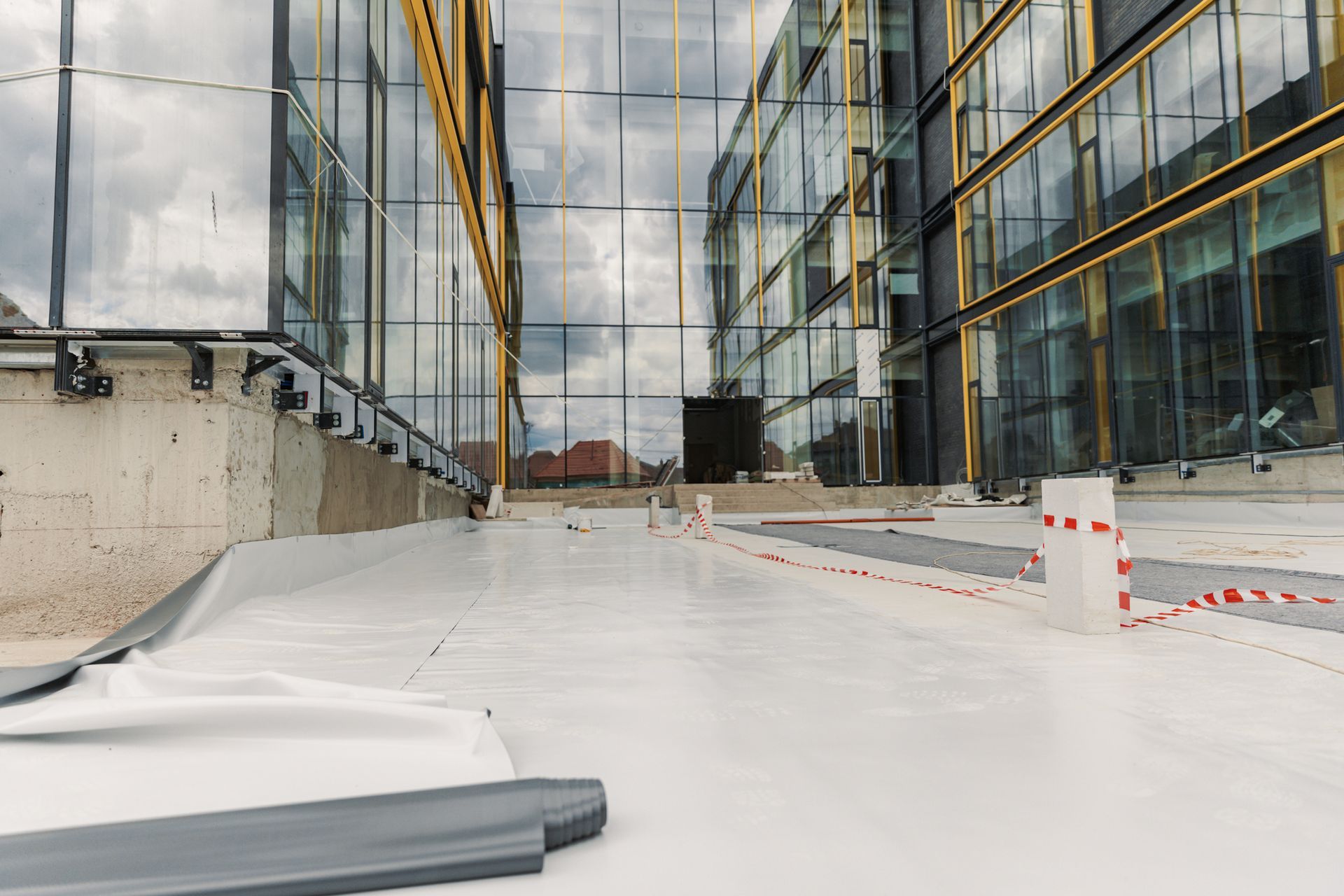 White roofing membrane on a building's rooftop, reflecting the glass facade. Construction in progress.