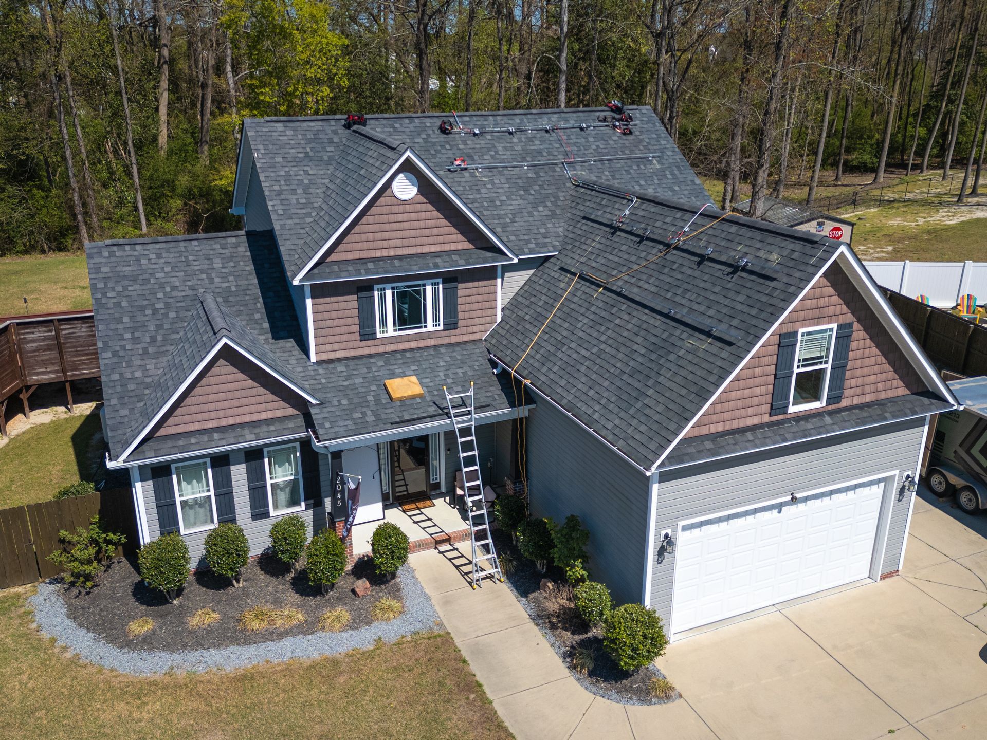 Aerial view of a two-story house with a new roof. Brown and gray color scheme. A ladder rests on the side.