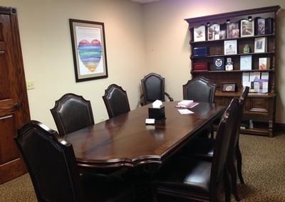 Conference room with a dark wood table, leather chairs, and a bookshelf against beige walls.