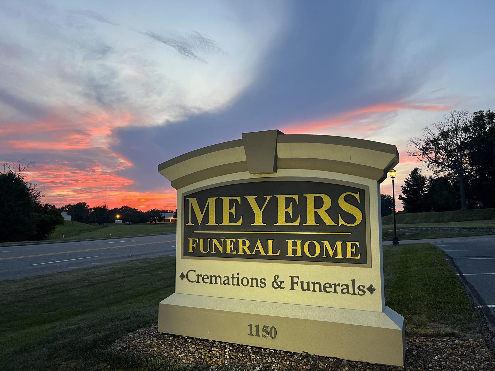 Meyers Funeral Home sign at dusk with pink clouds and a road in the background