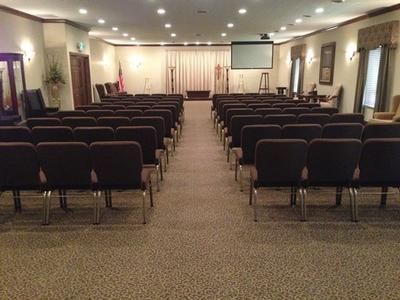 Empty conference room with rows of chairs facing a projector screen and stage area