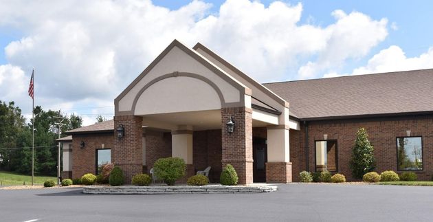 Brick building entrance with arched portico, white columns, and landscaped front drive