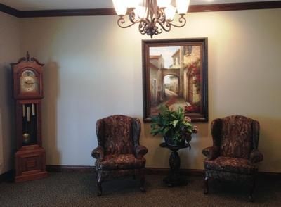 Elegant room with two patterned armchairs, a grandfather clock, a painting, and a potted plant under a chandelier