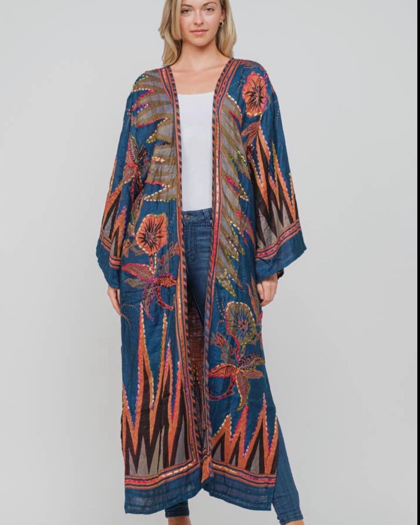 Woman wearing a long, open blue embroidered kimono over a white top and jeans.