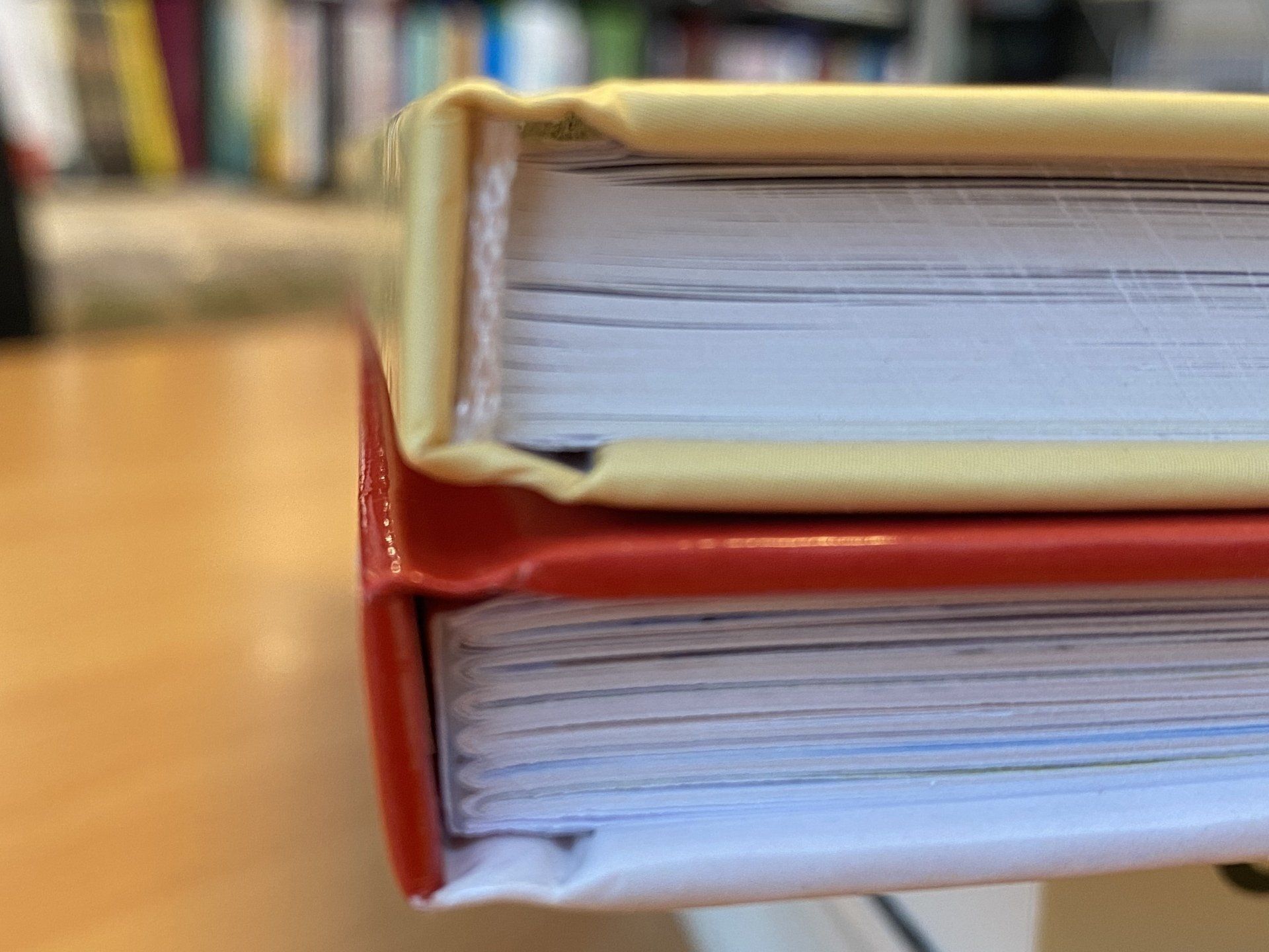 Op een plank staan ​​opgestapelde rode en beige hardcover boeken met witte bladzijderanden.