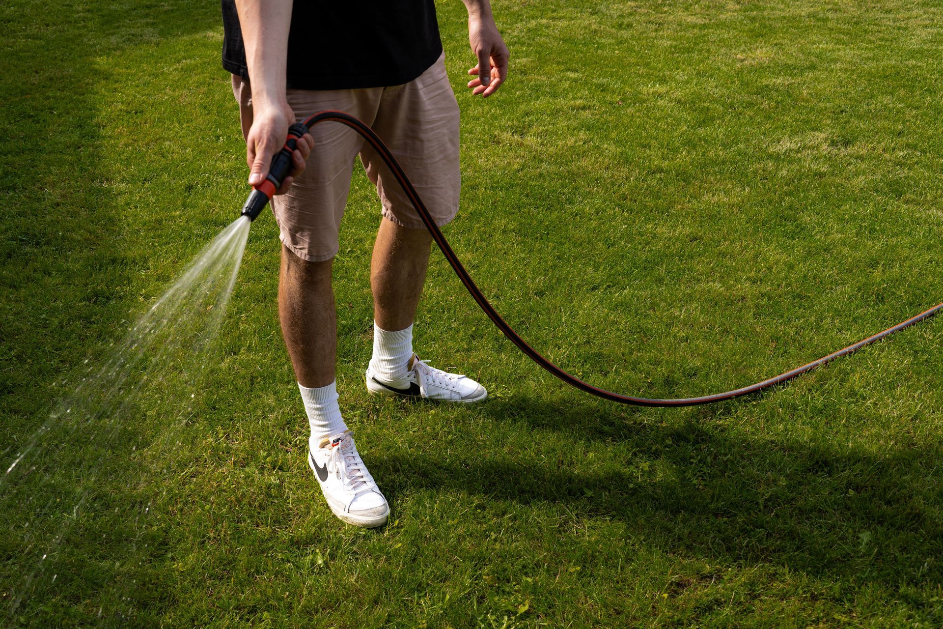 Man watering a green lawn with a garden hose