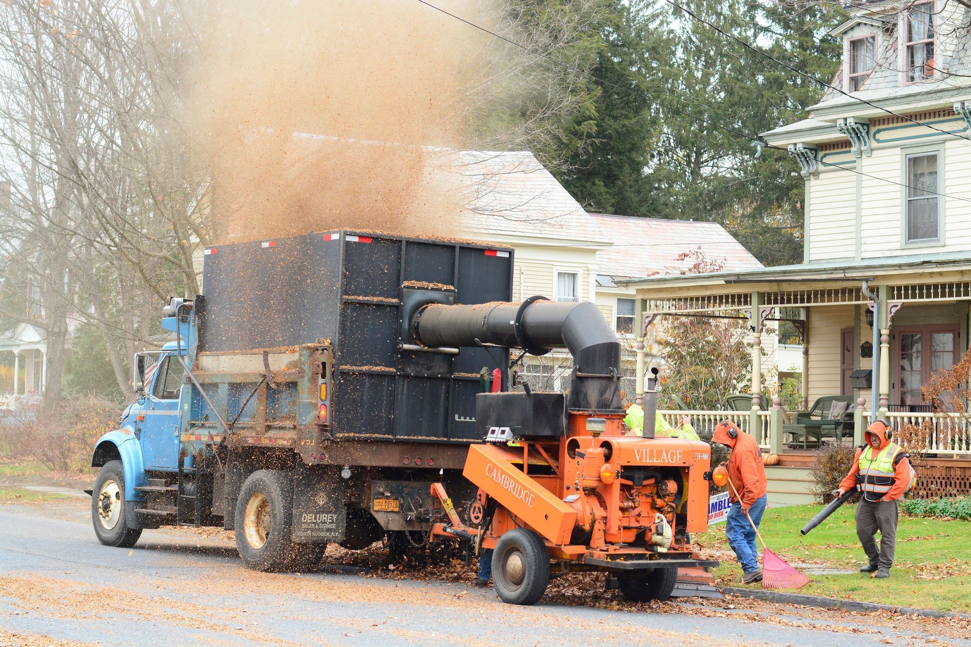 Crew collecting leaves with machinery on a residential street