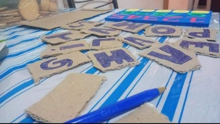 Letras de cartón con marcador azul sobre una mesa. Bolígrafo azul, números y más cartón.