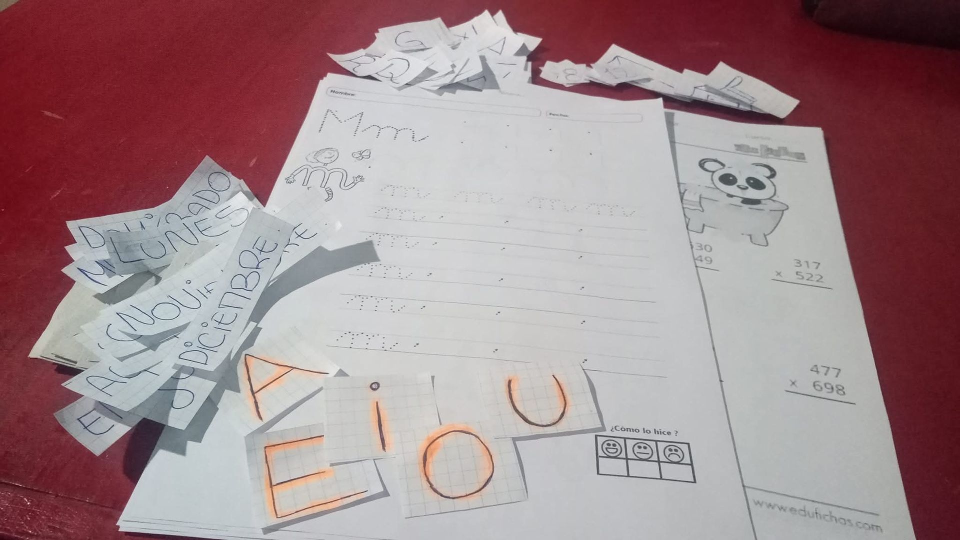 Papeles con recortes de letras, formas y un dibujo de panda sobre una superficie roja.
