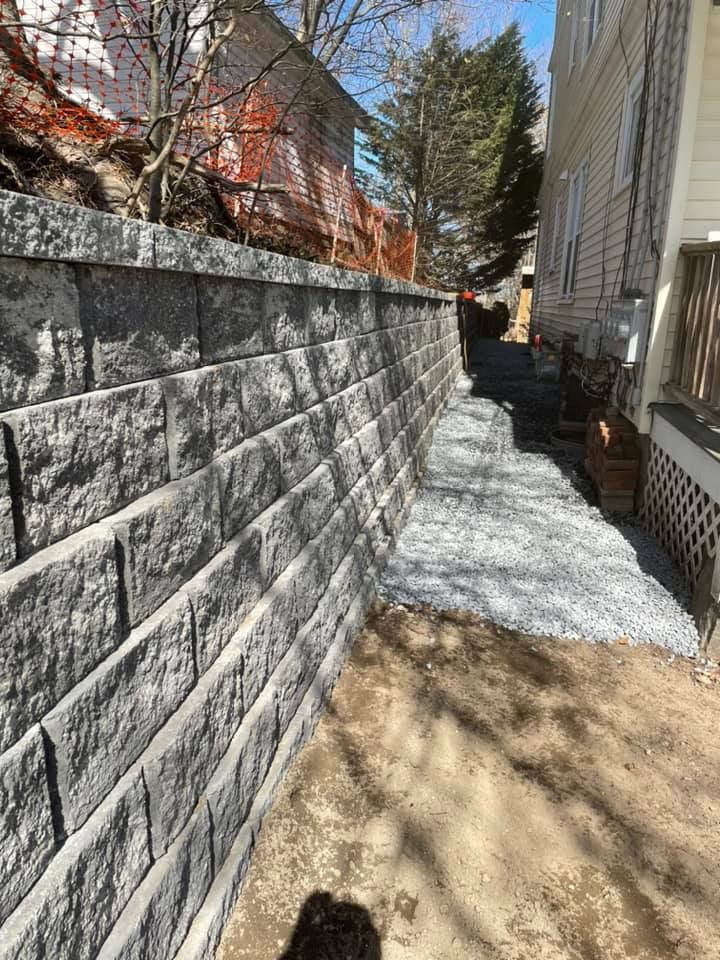 Gray retaining wall alongside a building and narrow pathway, under a bright sky.