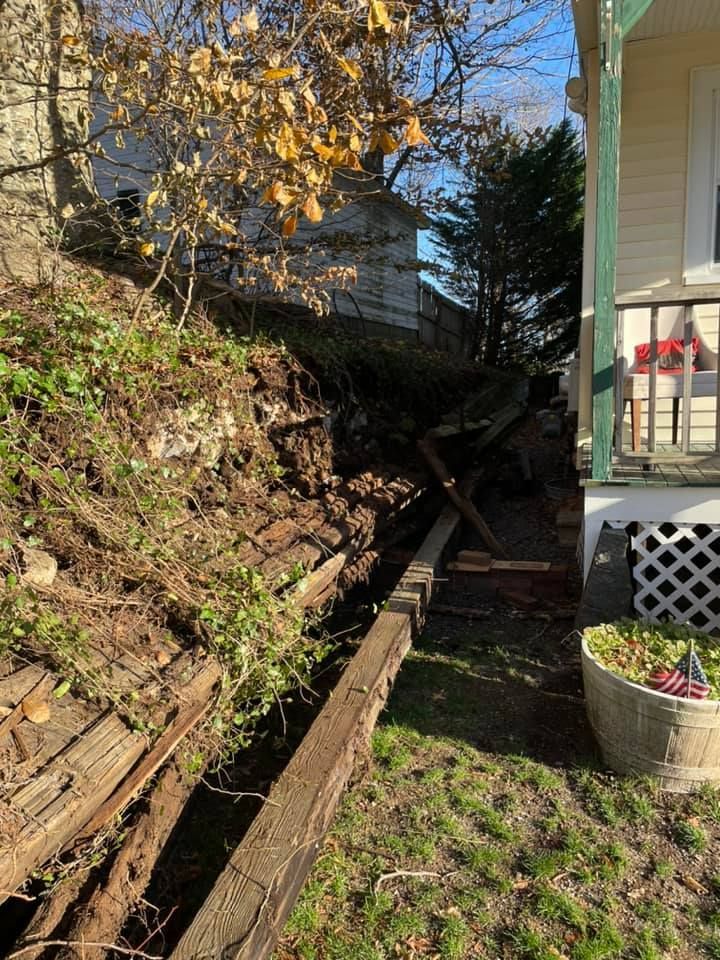 Damaged hillside with crumbling retaining wall next to a house.