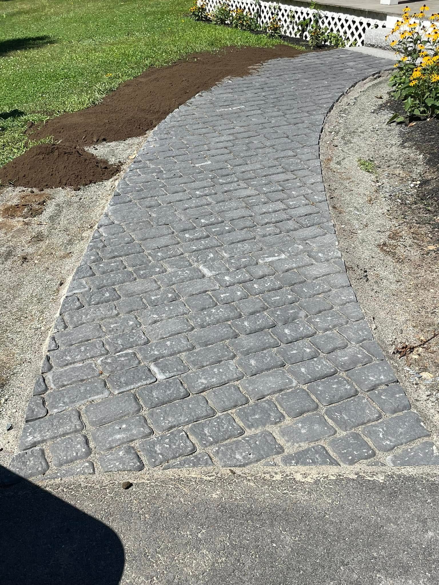 Brick pathway curves through a green yard. Brown dirt and gravel border the path.