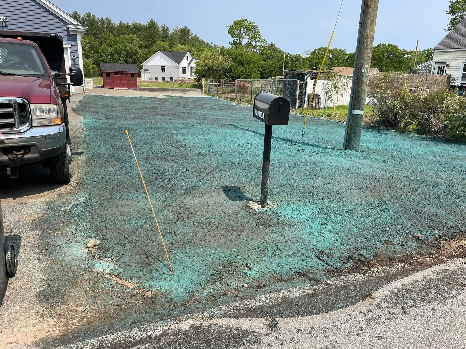 A gravel driveway with green seed. A black mailbox is centered. A truck is parked to the left.