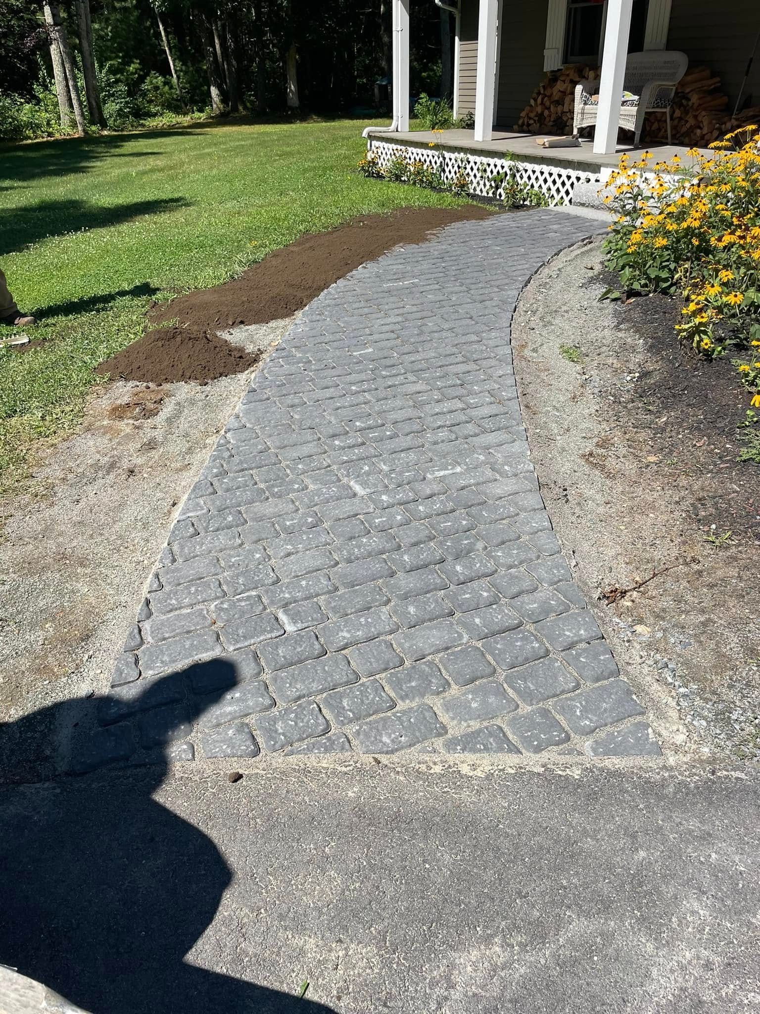 Gray brick pathway leads to a porch with a white railing.