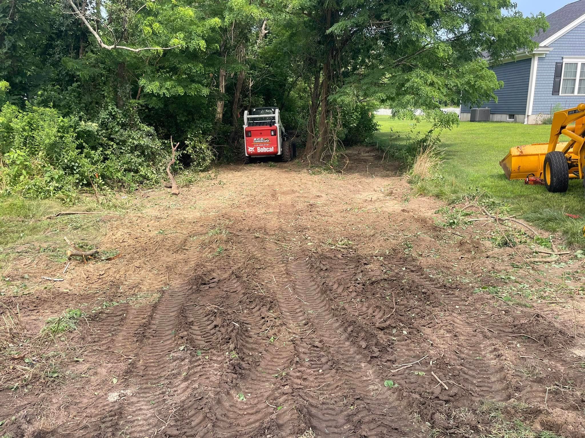 A red skid steer in a cleared area with trees; brown dirt path in front.