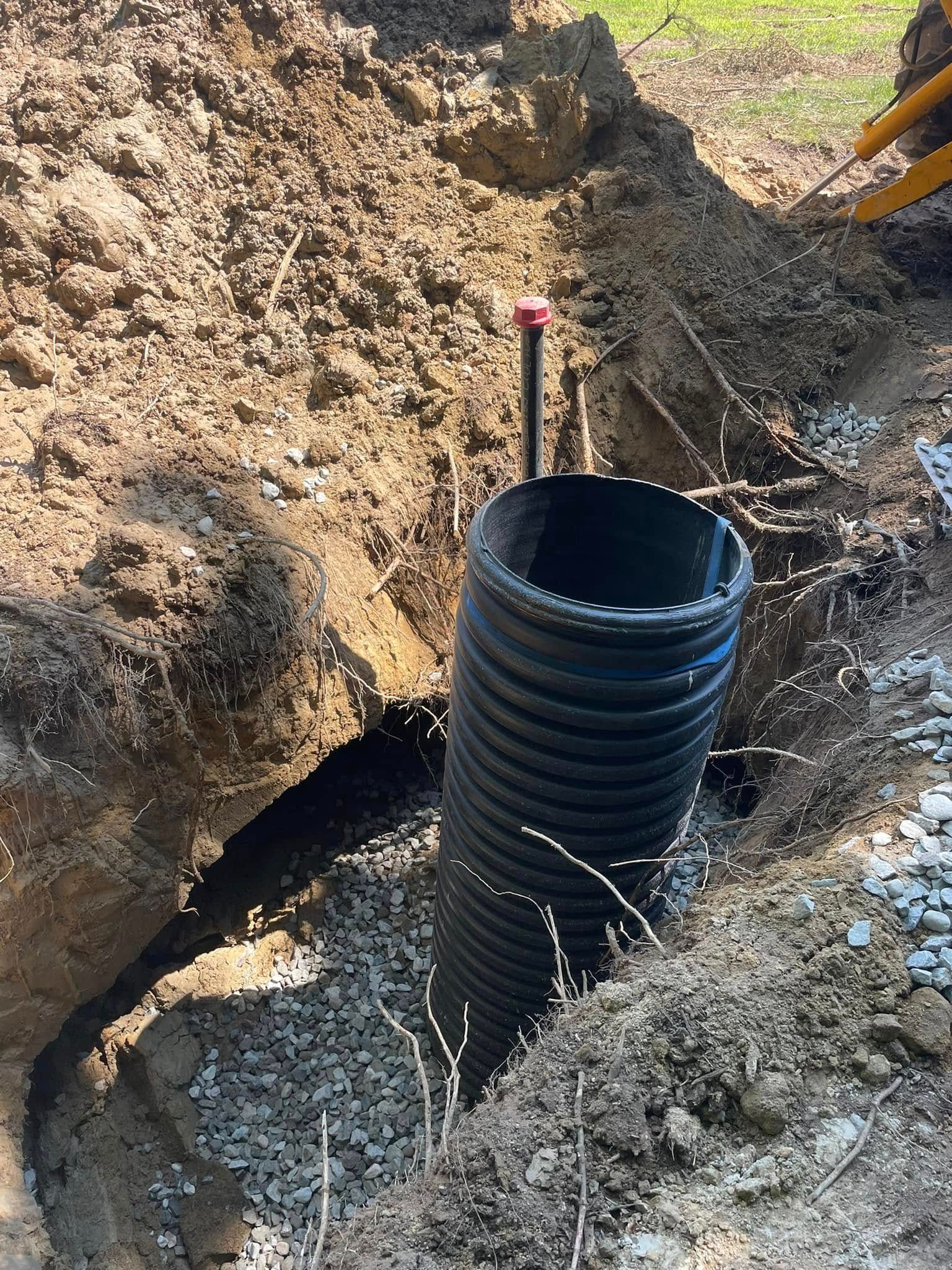 Black corrugated pipe in a dirt trench, with a red capped pipe emerging above ground.