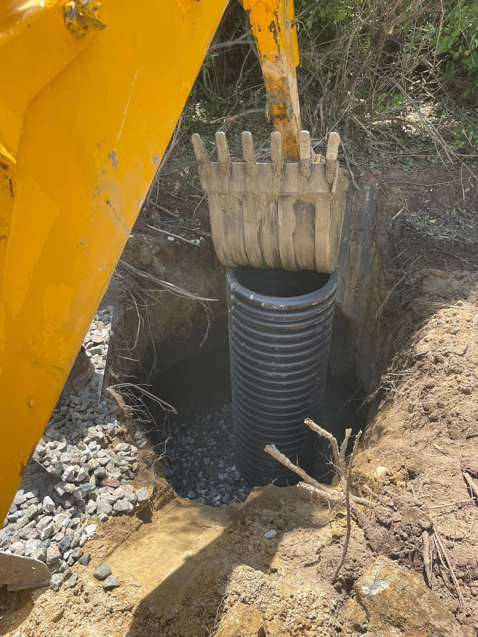 Yellow excavator placing corrugated black pipe into a trench.