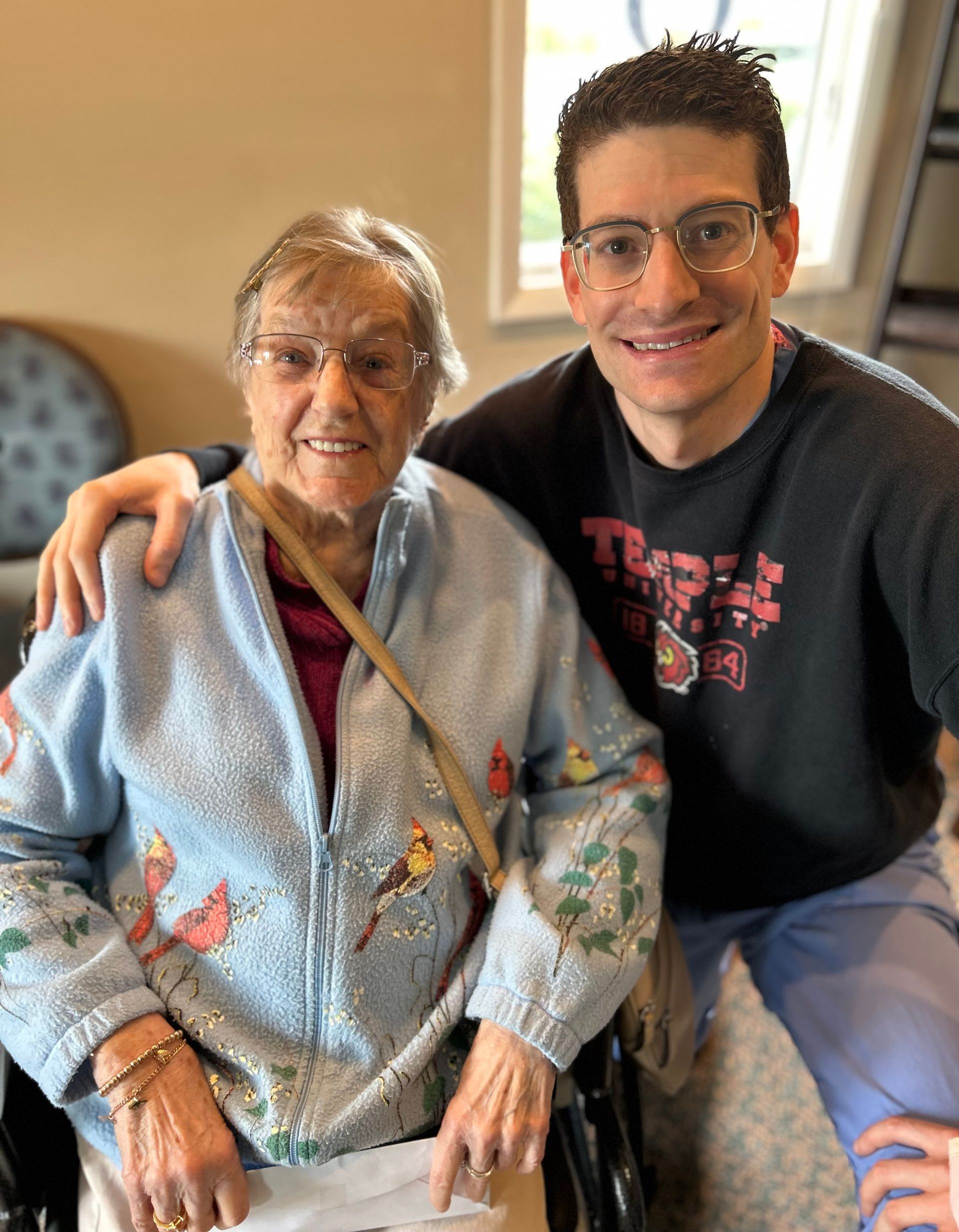 A man is sitting next to an elderly woman in a wheelchair.