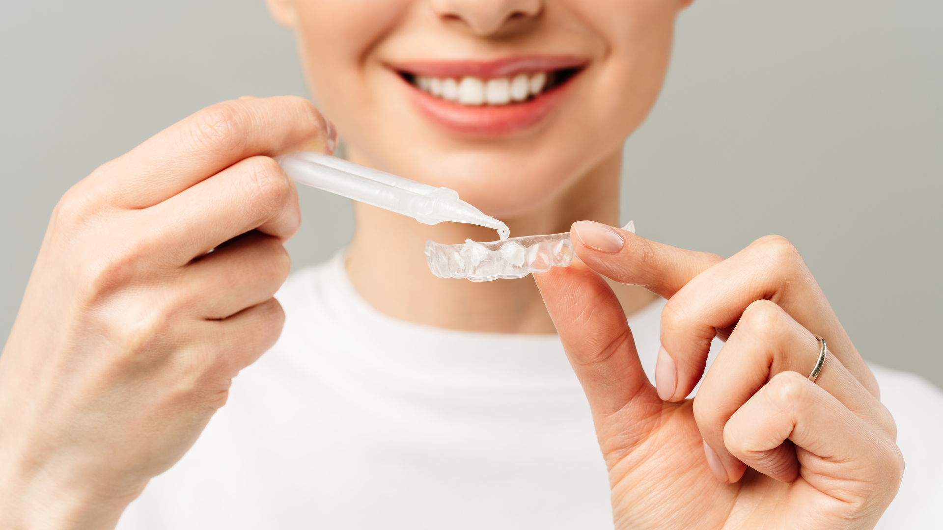 A woman is holding a tooth color chart in front of her teeth.