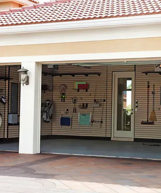 Garage interior with slat wall storage, various tools, and a door to the house.