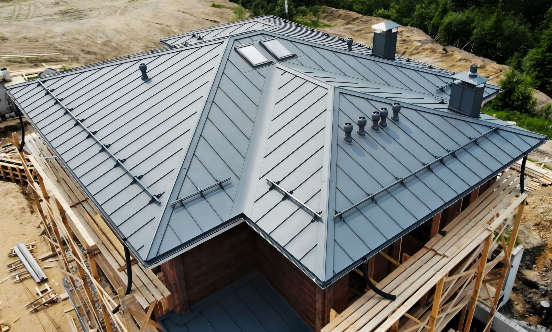 Aerial view of a newly installed gray metal roof on a house under construction.
