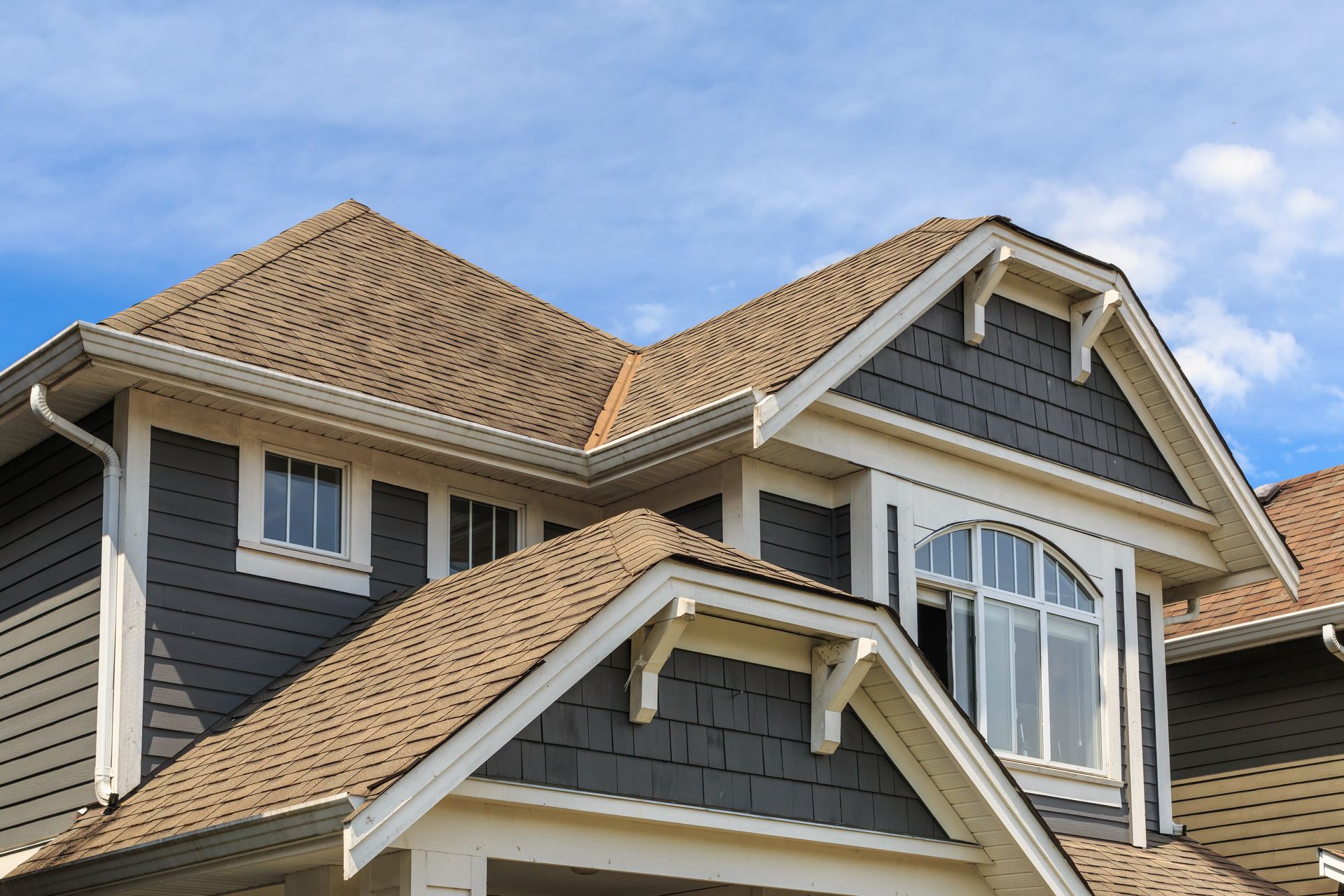 House exterior with gray siding, tan roof, and white trim against a blue sky. House exterior with gray siding, tan roof, and white trim against a blue sky.