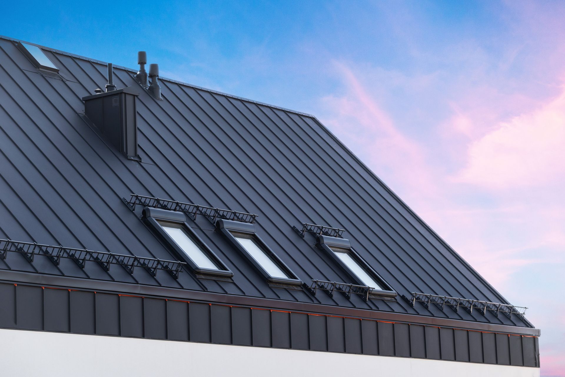 Black metal roof with skylights and chimney against a blue and pink sky. Black metal roof with skylights and chimney against a blue and pink sky.