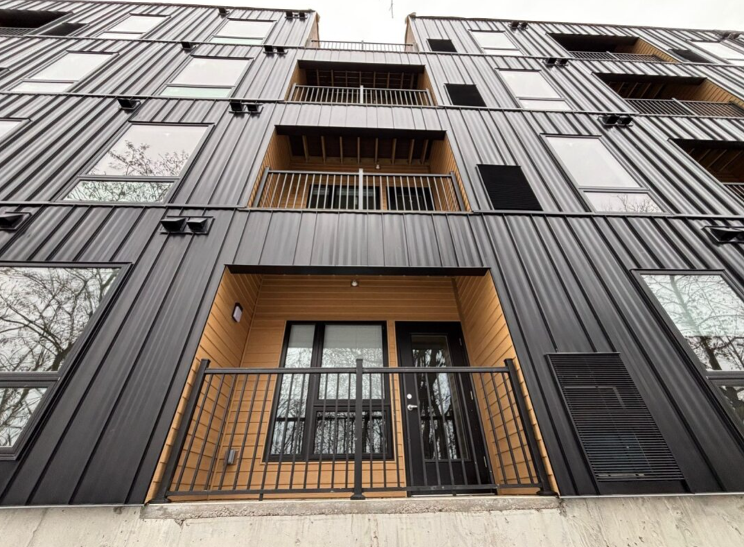 Modern black building facade with wood balconies and large windows, viewed from below