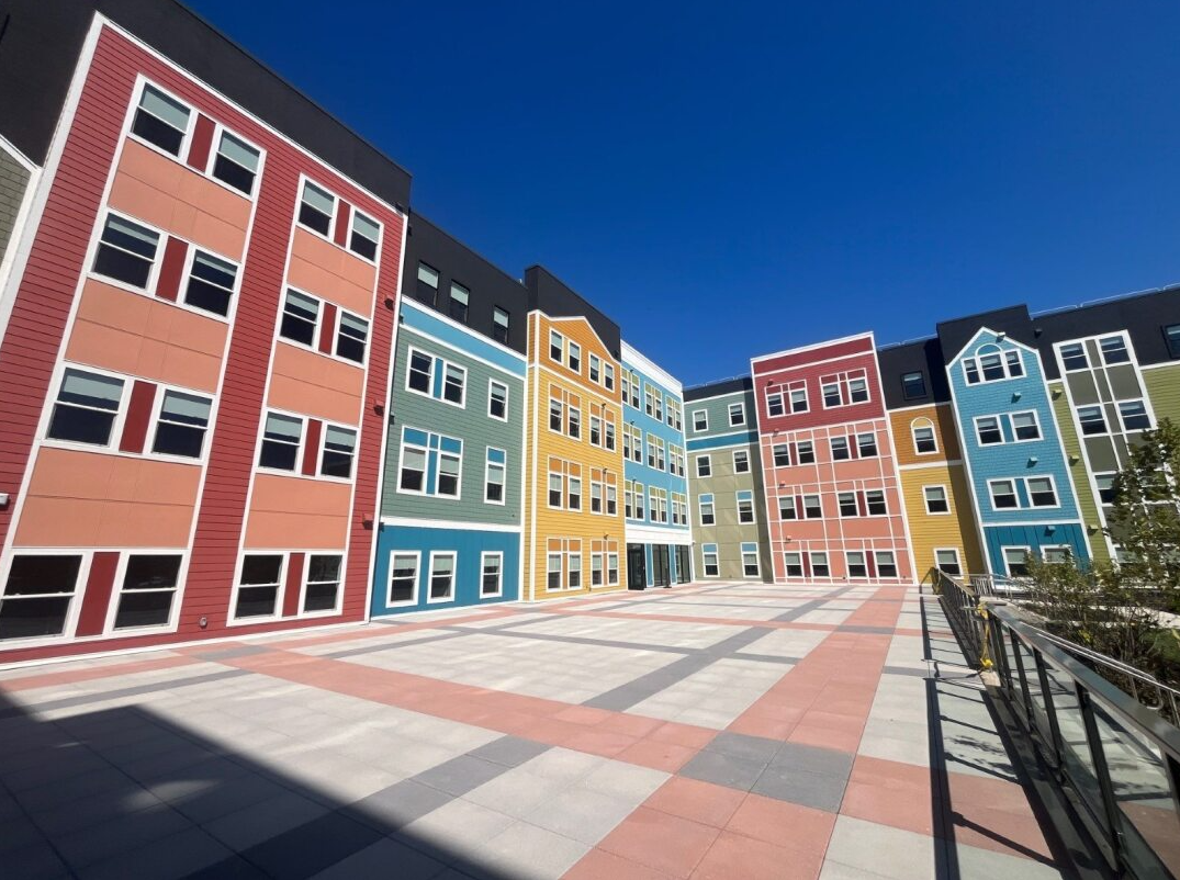 Colorful row of apartment buildings around a wide paved courtyard under a clear blue sky.