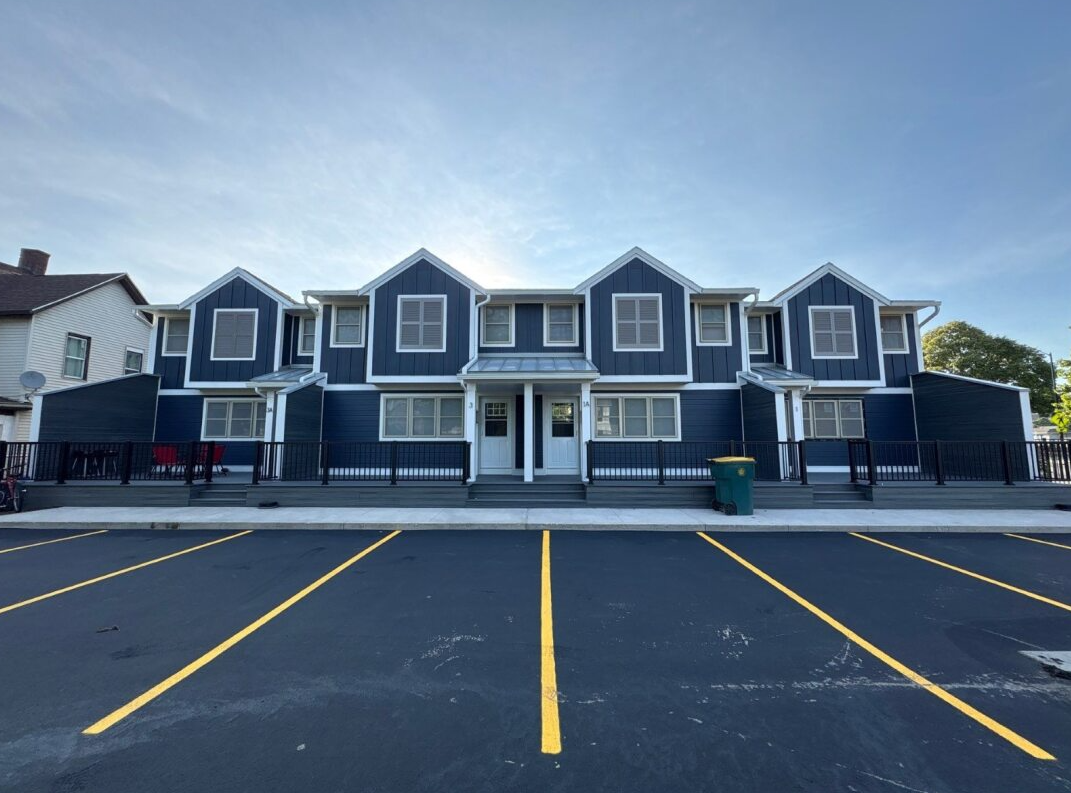 Row of blue-gray townhouses with white trim behind an empty parking lot at dawn