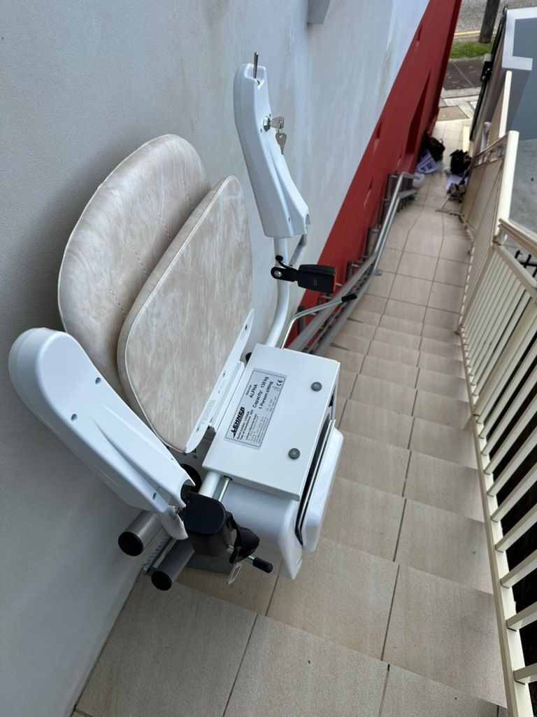 A person sitting in a stairlift, wearing a grey seatbelt secured by a red buckle.