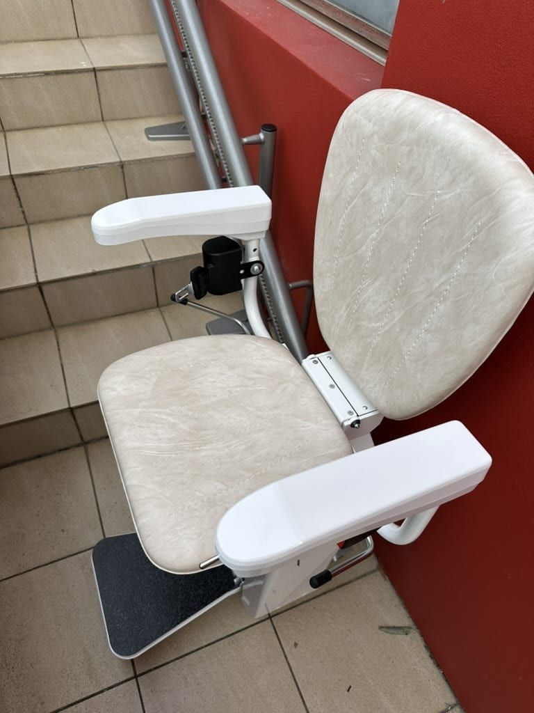 White stair lift chair with armrests on a tiled staircase indoors