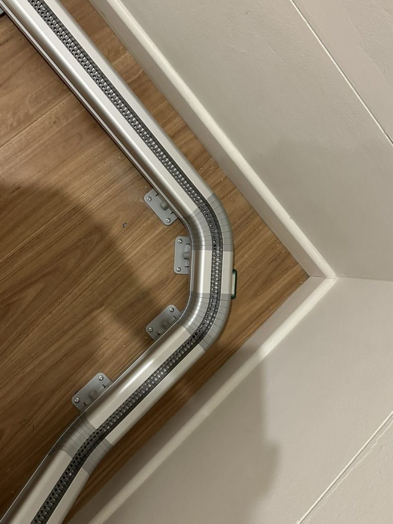 Metal pipe with cable tray running along a corner wall above a wooden floor.