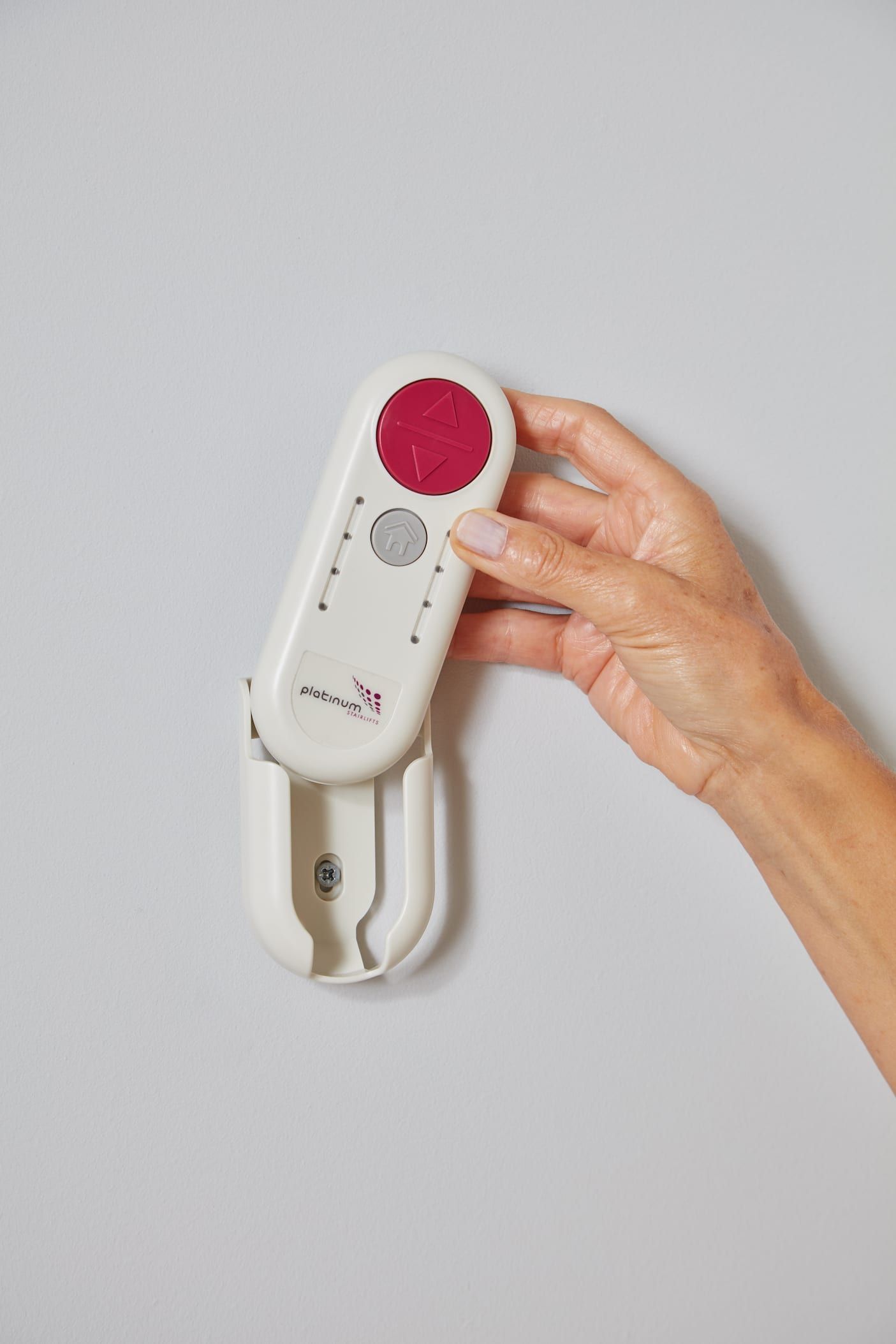 Hand holding a white corded emergency alarm with a red button against a gray wall