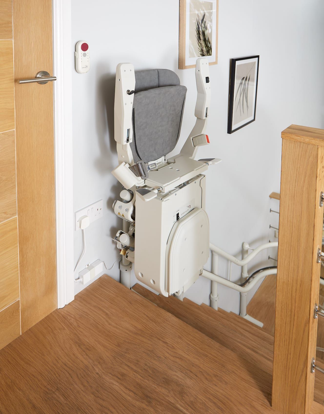 Indoor stairlift beside a wooden staircase in a home hallway with a wall-mounted control panel.